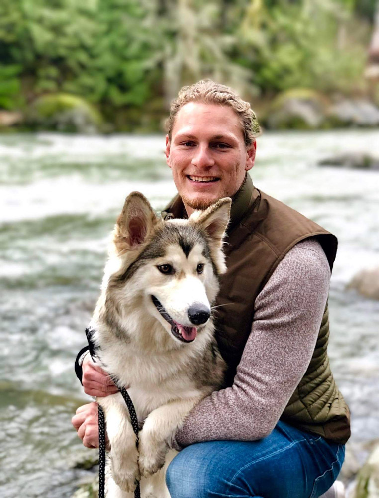 Cole bio photo Winemaker Cole, holding a large dog with a river in the background